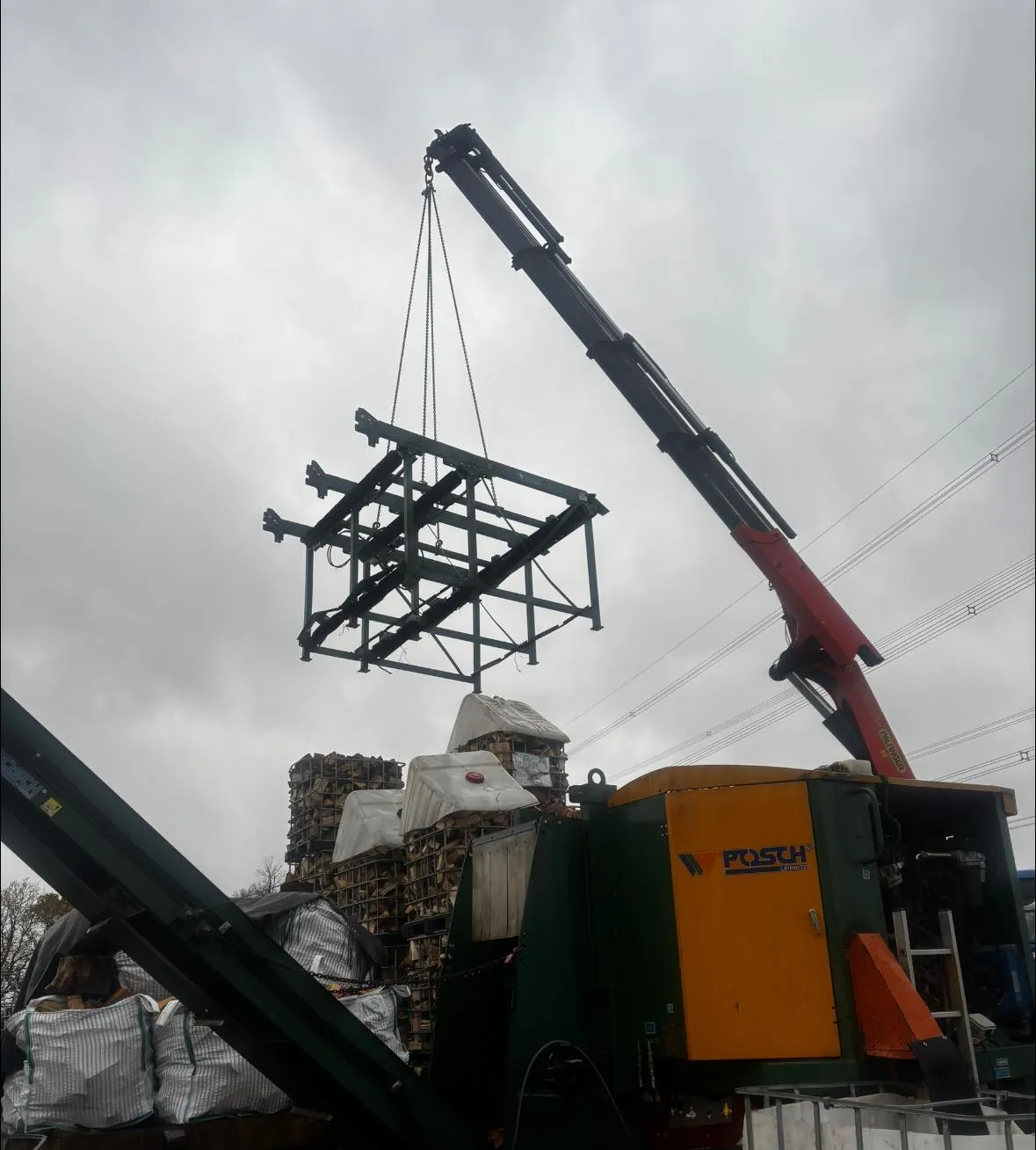 A crane lifting a steel log-stacking frame above the barn