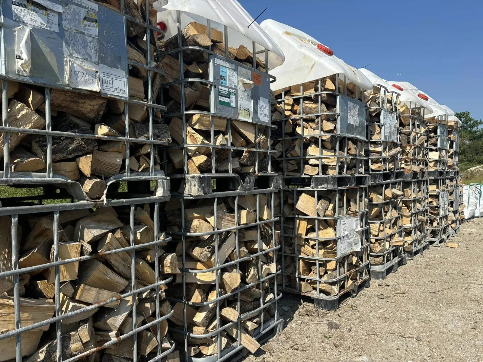 Rows of wire crates packed with split logs, stacked in a line outside.