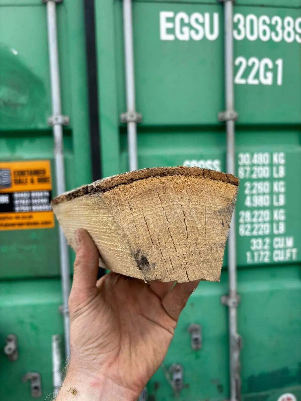 A hand holds up a single split log, showing the cut end grain.