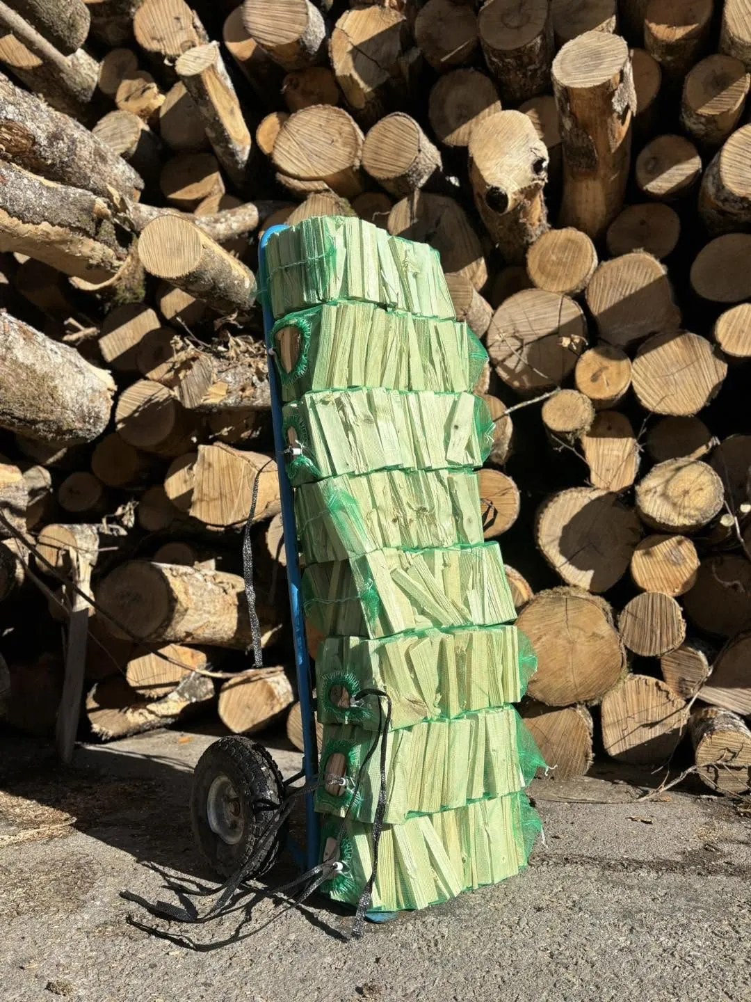 Kindling nets stacked on a hand trolley, with a log pile behind.