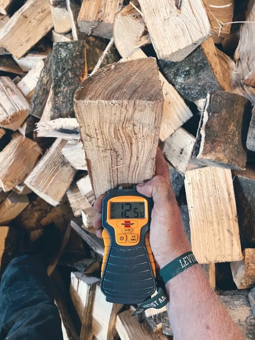 A moisture meter reads 12.5% on a split log held against the pile.