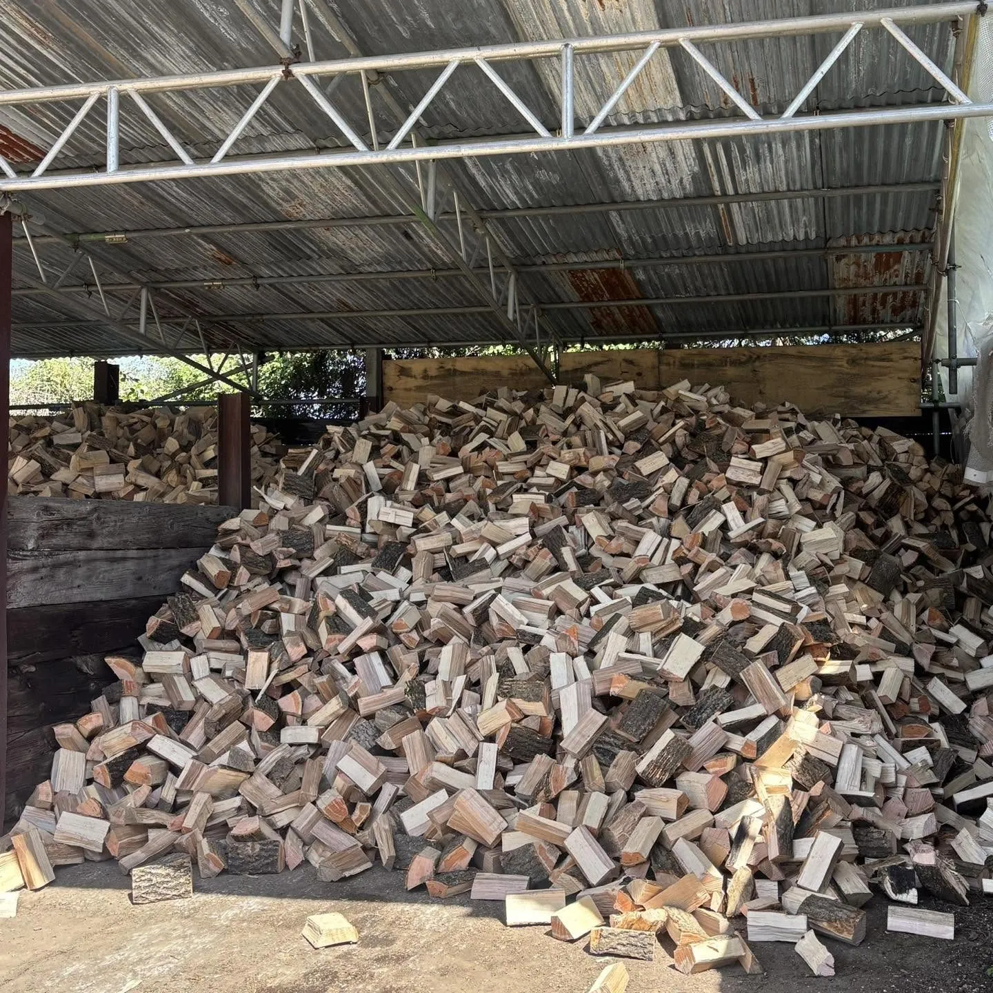 A large heap of split logs piled up under a barn roof.