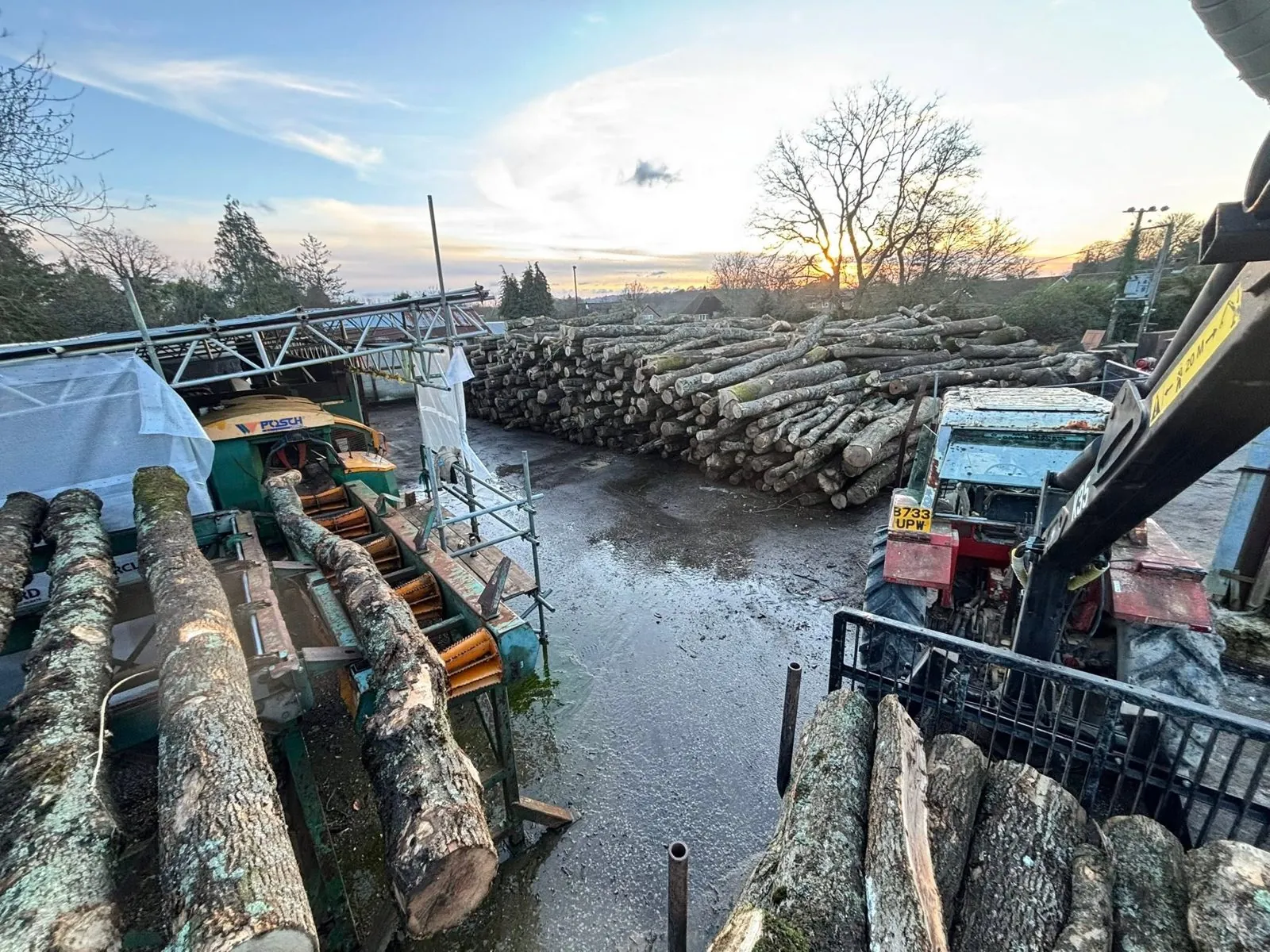 Timber stacked in the yard at sunset, with machinery around the edges.