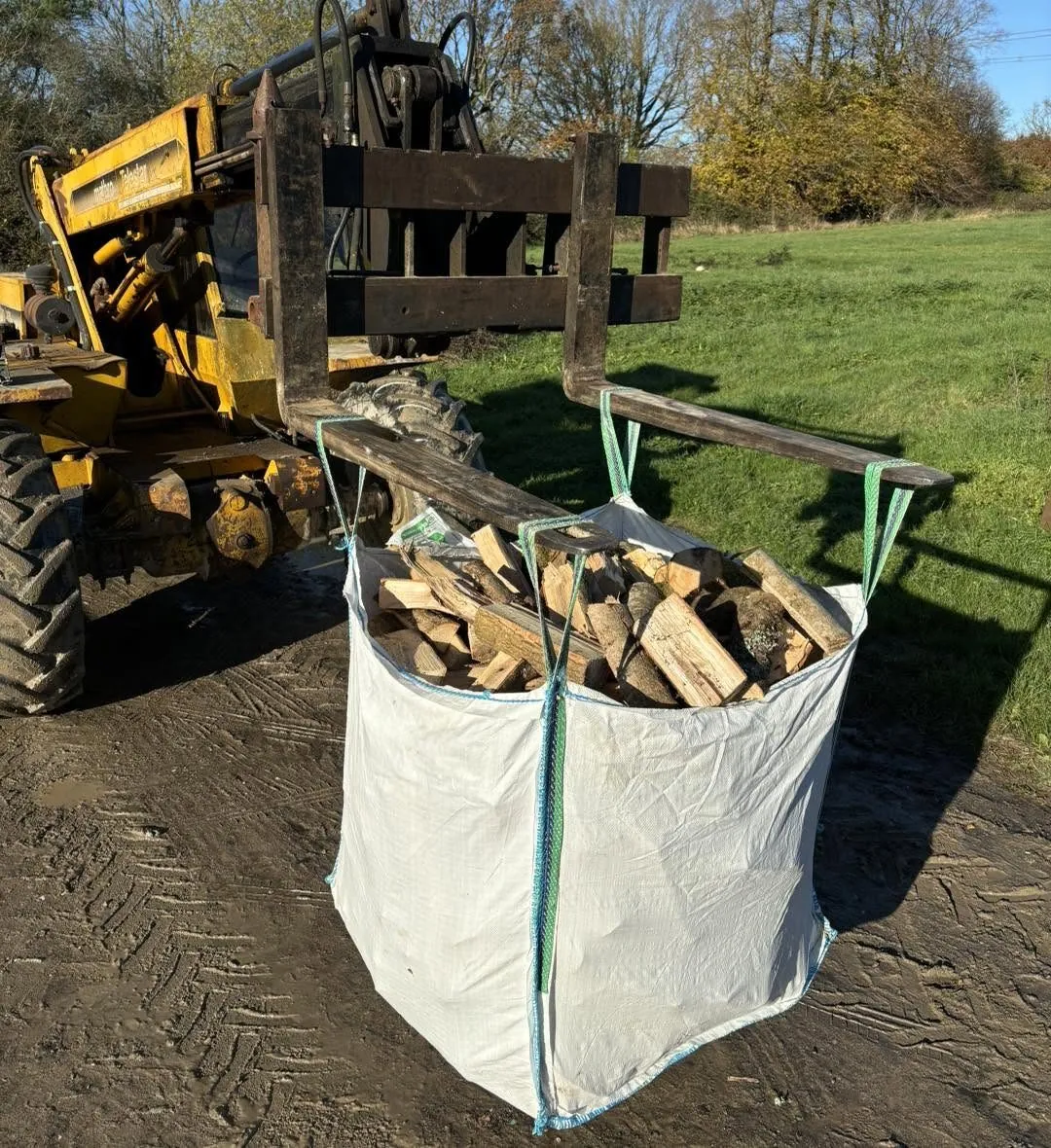 A bag of split logs lifted on forklift forks, with a field behind.