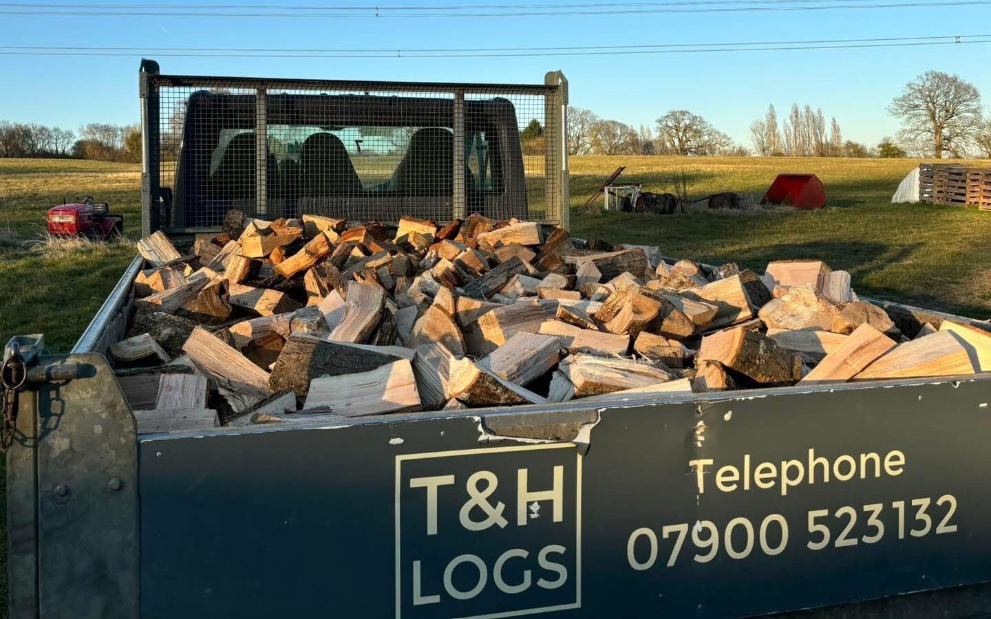 A T&H Logs branded 3.5t tipper loaded with split seasoned hardwood in a West Sussex field